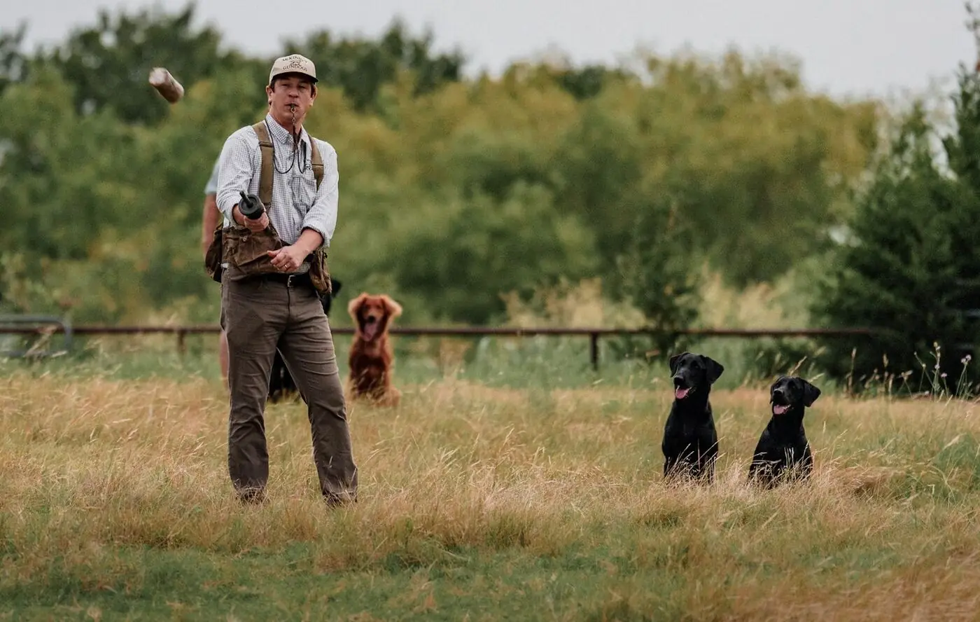Cole McKinney working a black Labrador with a whistle and lead in the field